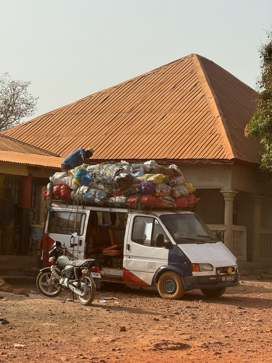 A person loads sacks onto a cargo van on a dusty street.