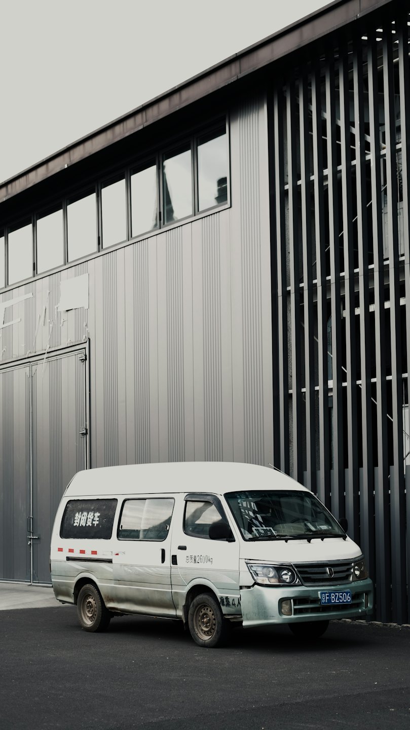 A white cargo van parked in front of a modern industrial building.